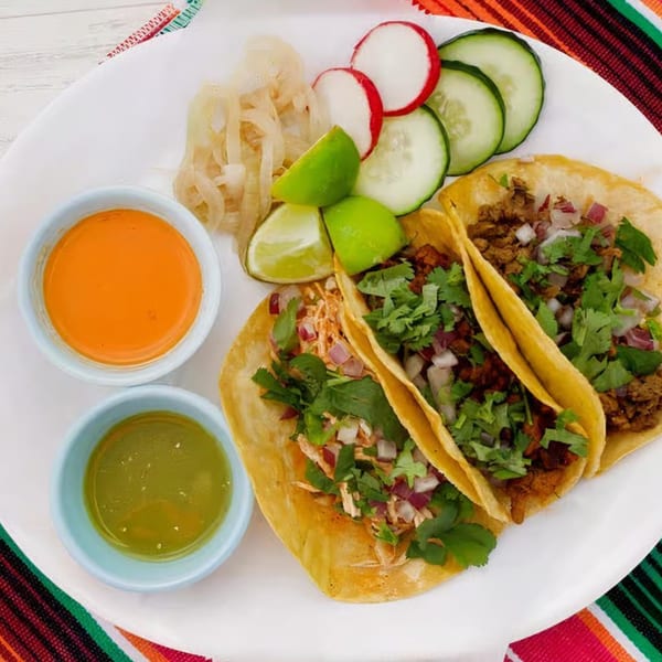 Three Nunez Foods tacos with cilantro, onions, lime, radishes, cucumbers, and two sauces.
