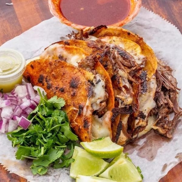 Nunez Foods birria tacos with melted cheese, cilantro, red onions, lime wedges, and consommé.