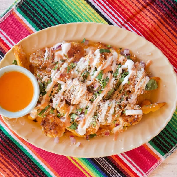 Nunez Foods' Mexican shrimp fries with sauce, cheese, cilantro, and red onions on a colorful striped placemat.